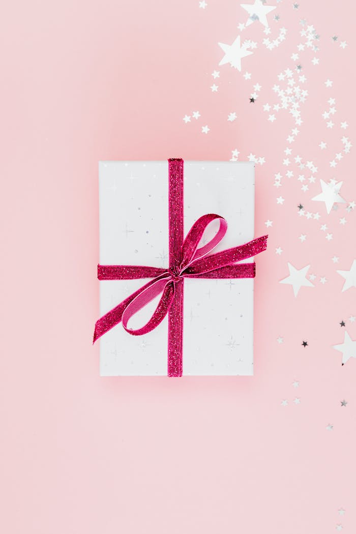 Top view of a wrapped gift with pink ribbon on a pink background, ideal for celebrations.